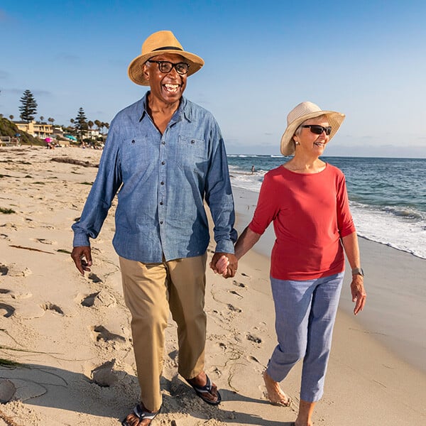 Senior couple wearing sun hats holding hands and walking on the beach