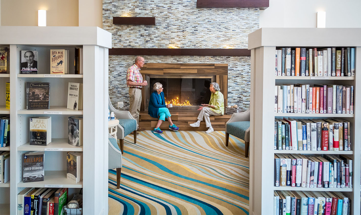 Three seniors by the fireplace inside the community library