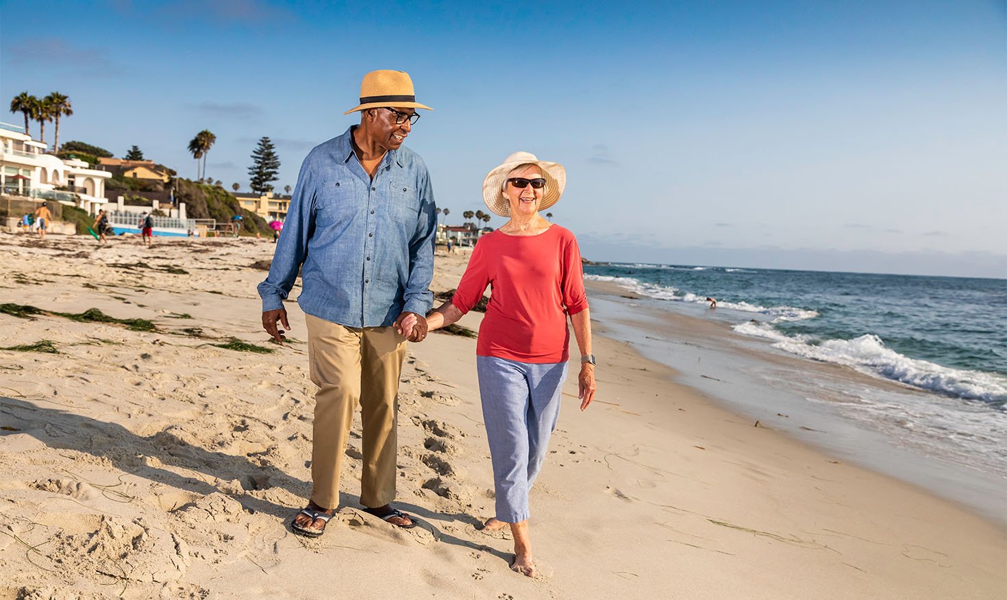 Senior couple wearing sun hats holding hands and walking on the beach