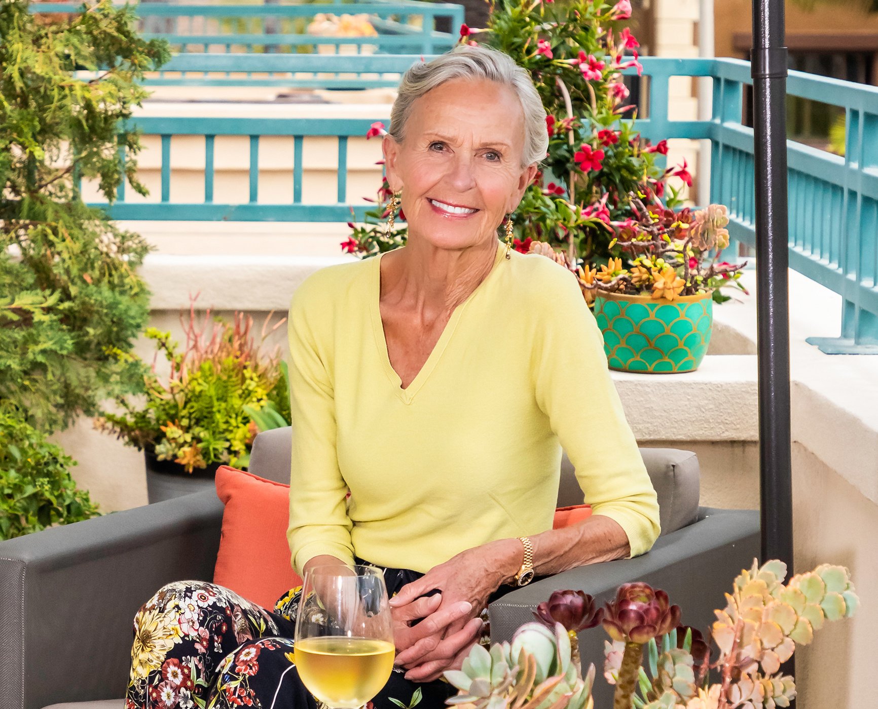 Senior woman sitting outside on private balcony with a glass of white wine