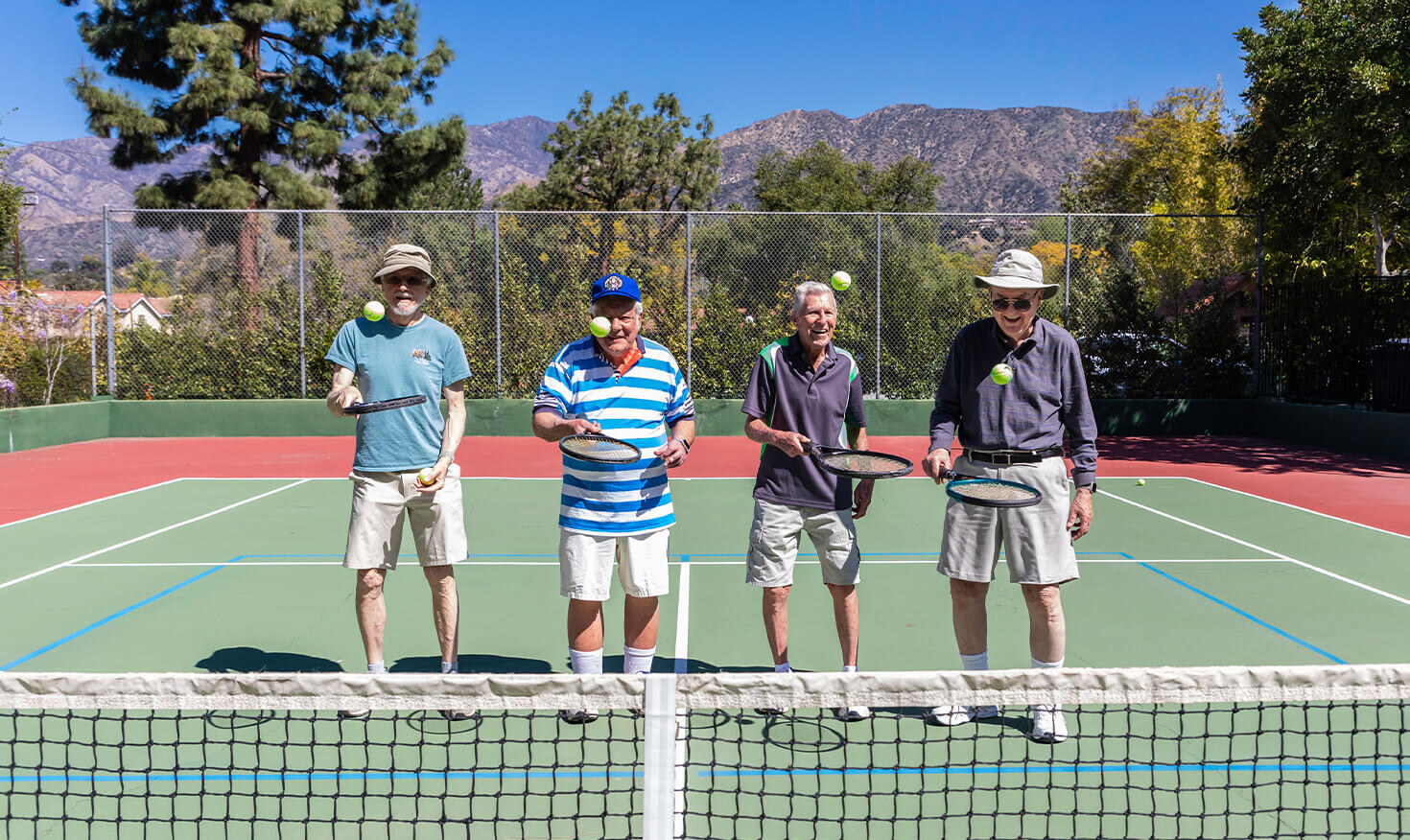 Four senior men bouncing tennis balls on their rackets on the Westminster Gardens tennis court