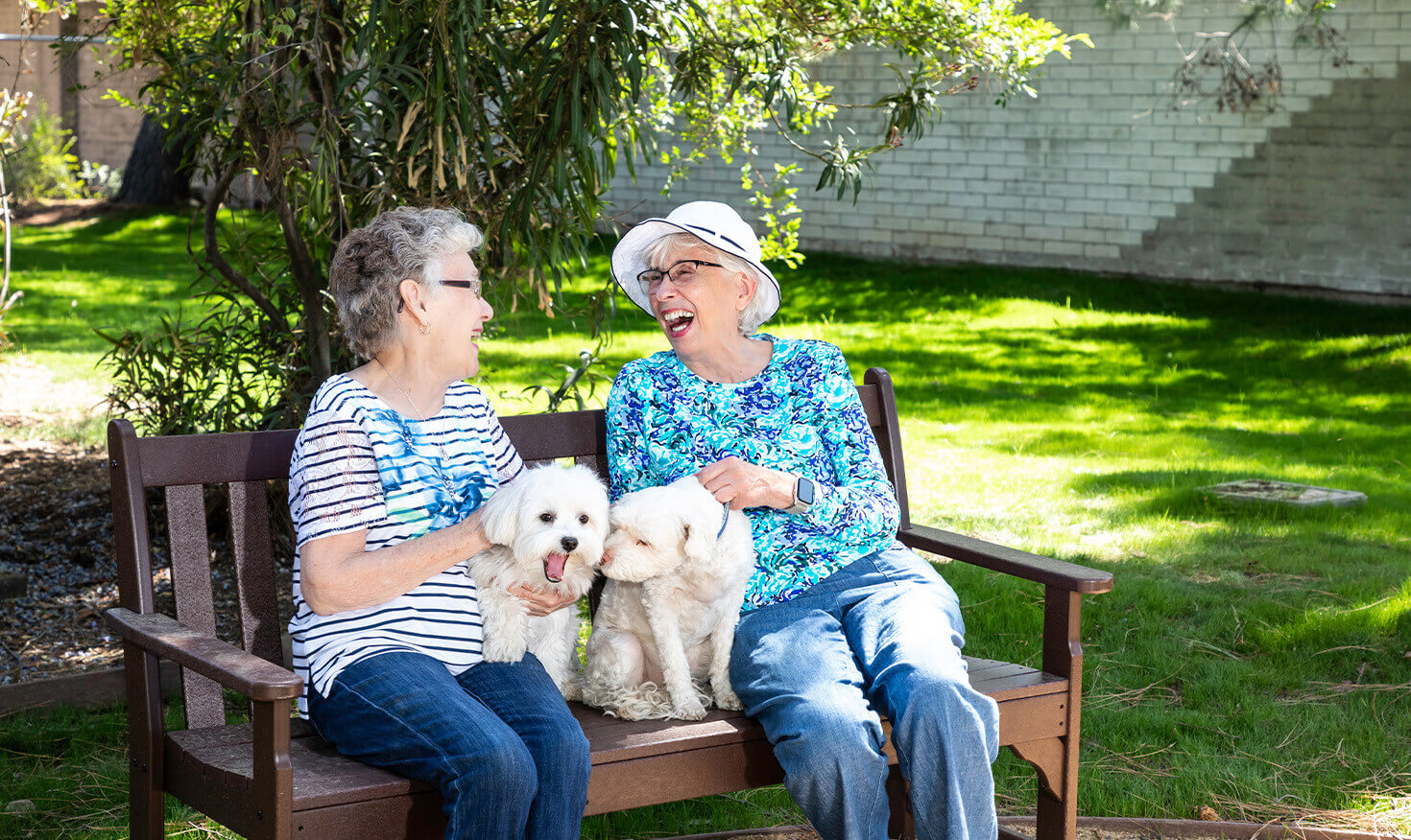 Two senior women and their small white dogs sitting on an outdoor bench at Westminster Gardens