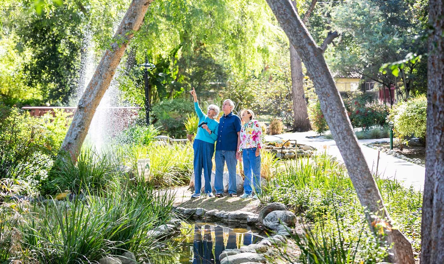 Two senior women — one pointing up — and a senior man next to the pond at Westminster Gardens