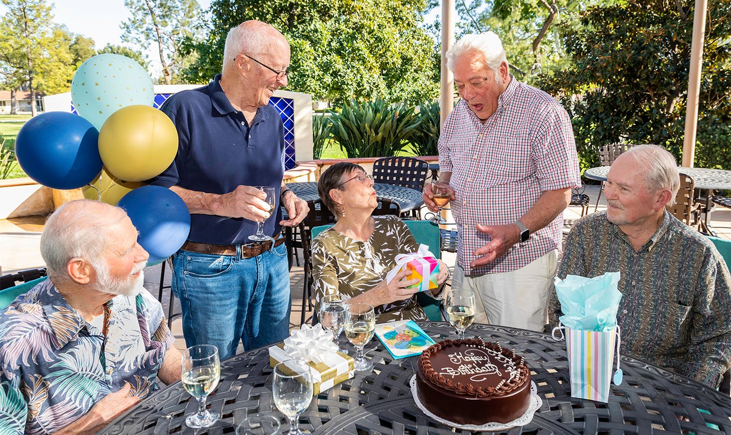 Four senior men and a senior woman celebrating a birthday on a patio at Westminster Gardens