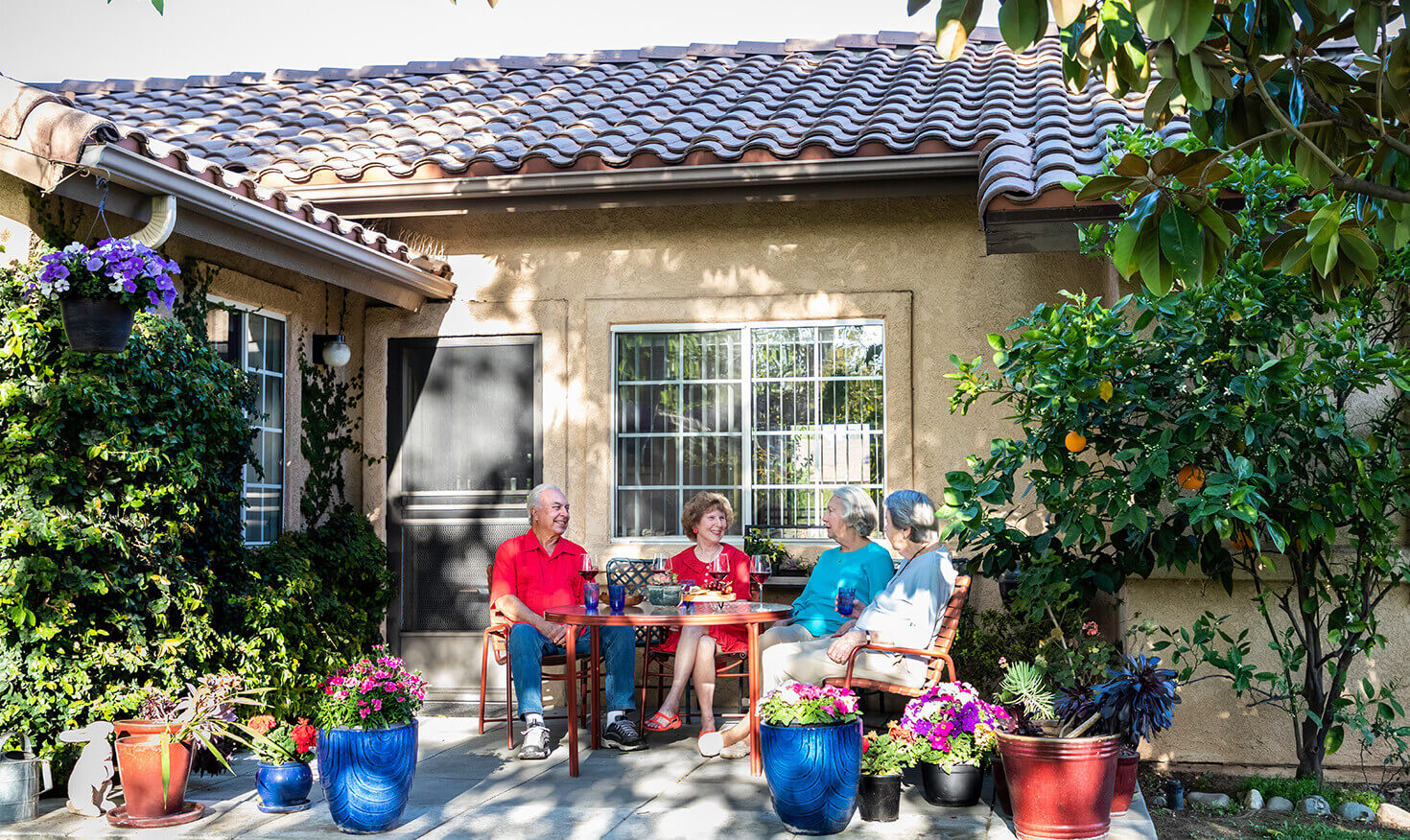 Four seniors, surrounded by plants, sitting at a table on the patio of a home at Westminster Gardens