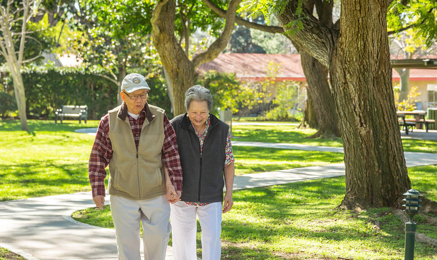 Senior couple holding hands and walking on a paved path through the grounds of Westminster Gardens