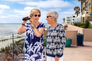 Two senior women looking out at the beach with binoculars