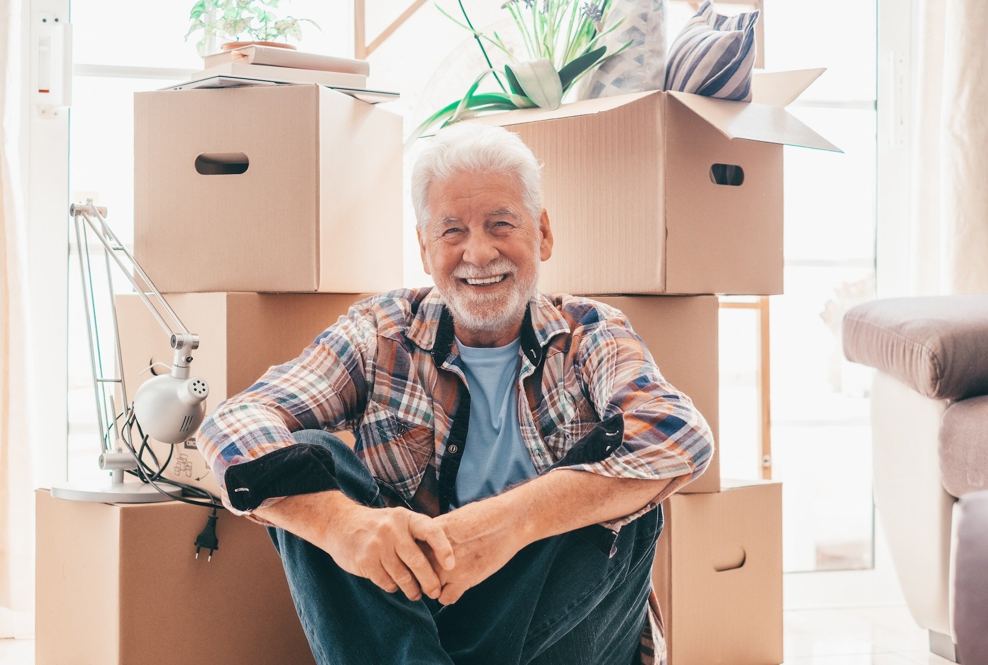 senior man smiling and sitting on floor in front of moving boxes