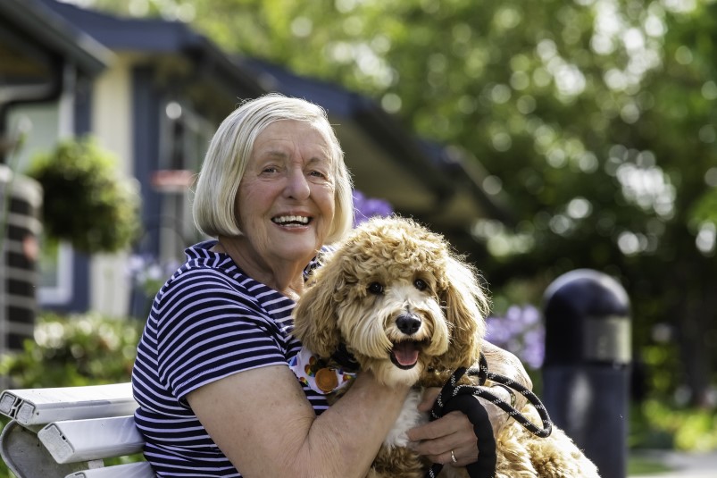 Senior woman holding dog while sitting on an outdoor bench at Redwood Terrace