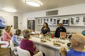 Group of seniors sitting at a kitchen island with ingredients set out on it for a cooking class