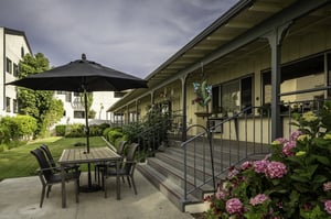 Patio table and chairs with umbrella at the bottom of the stairs leading to apartment homes at Redwood Terrace