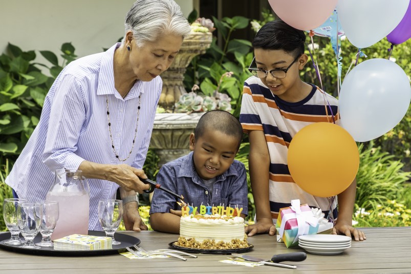 Senior woman lighting candles on a birthday cake on the table in front of her grandson