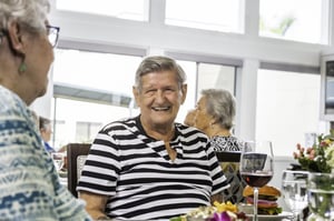 Senior man smiling at a senior woman as they sit in the dining room at Redwood Terrace