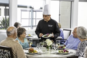 Redwood Terrace chef presenting a plate of food to a senior resident in the community dining room