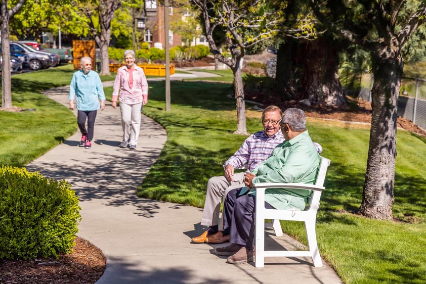 Two senior men sitting on a park bench and two senior women walking along the sidewalk