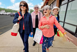 Group of four senior women walking outside with shopping bags