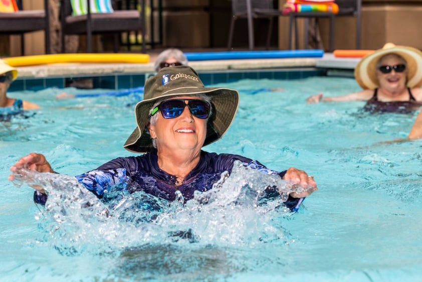 Senior woman wearing a sun hat doing water exercises in an outdoor pool