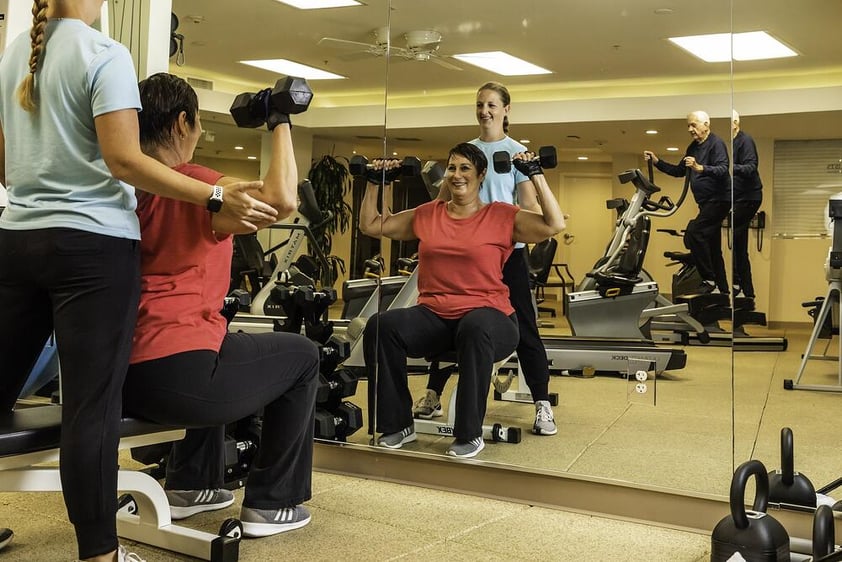 Senior woman lifting weights with the help of a trainer in the White Sands fitness center