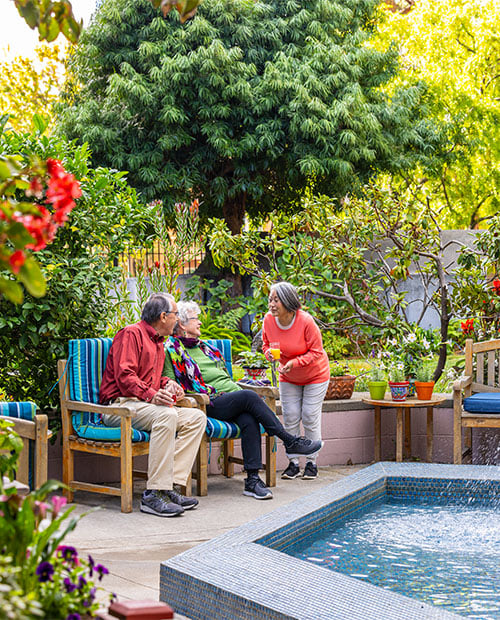 Senior woman standing and talking to a senior couple sitting in an outdoor seating area at Piedmont Gardens