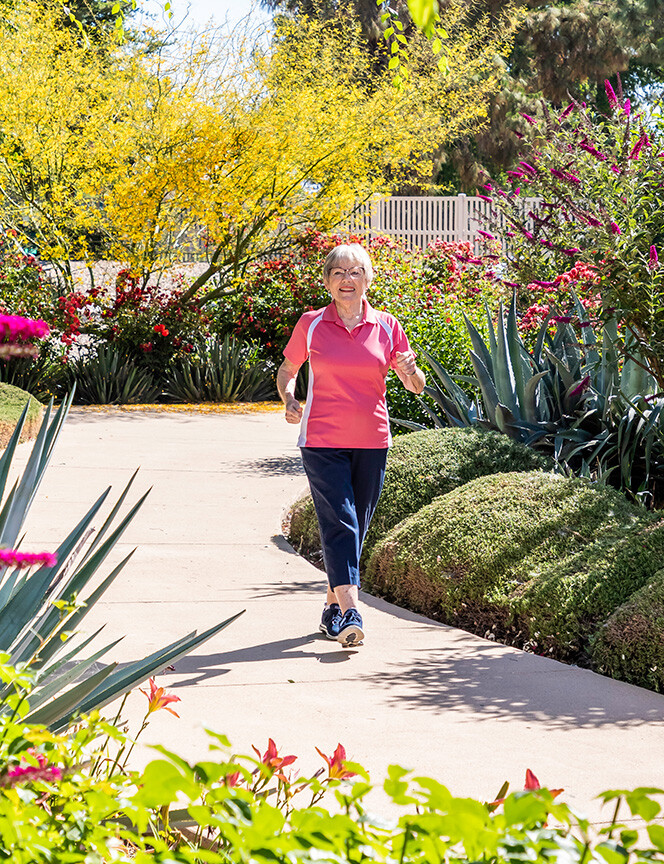 Senior woman walking on a sidewalk through the garden at Rosewood