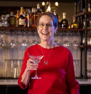 Smiling senior woman holding up a martini glass in front of a bar