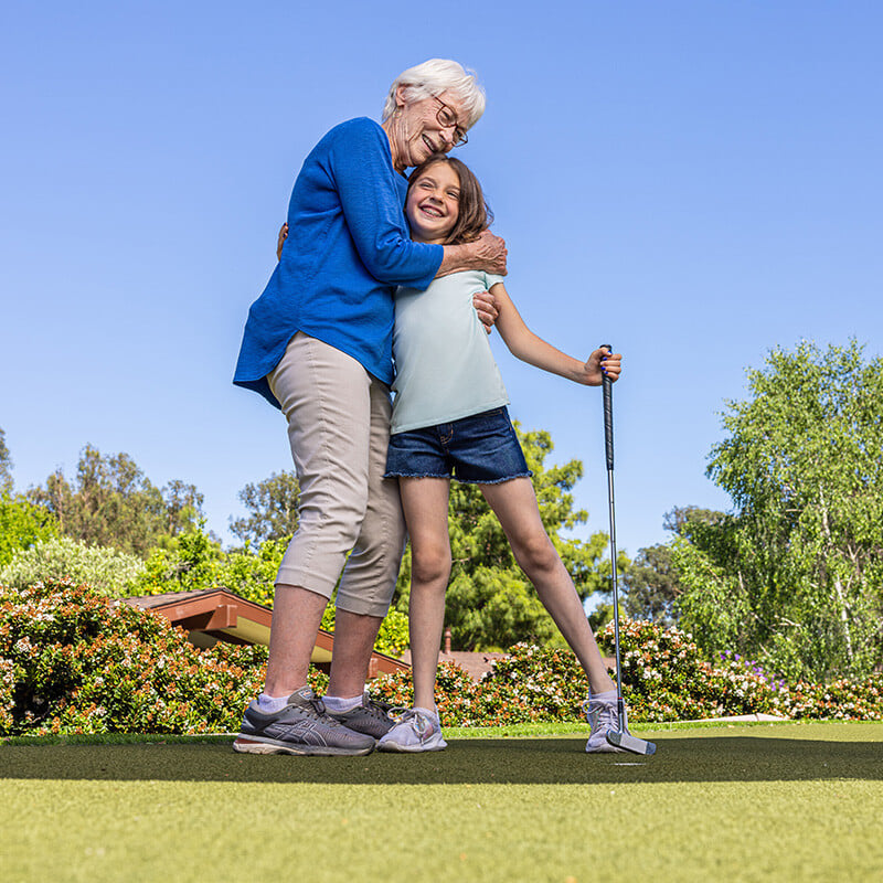 Senior woman hugging young girl who is holding a putter