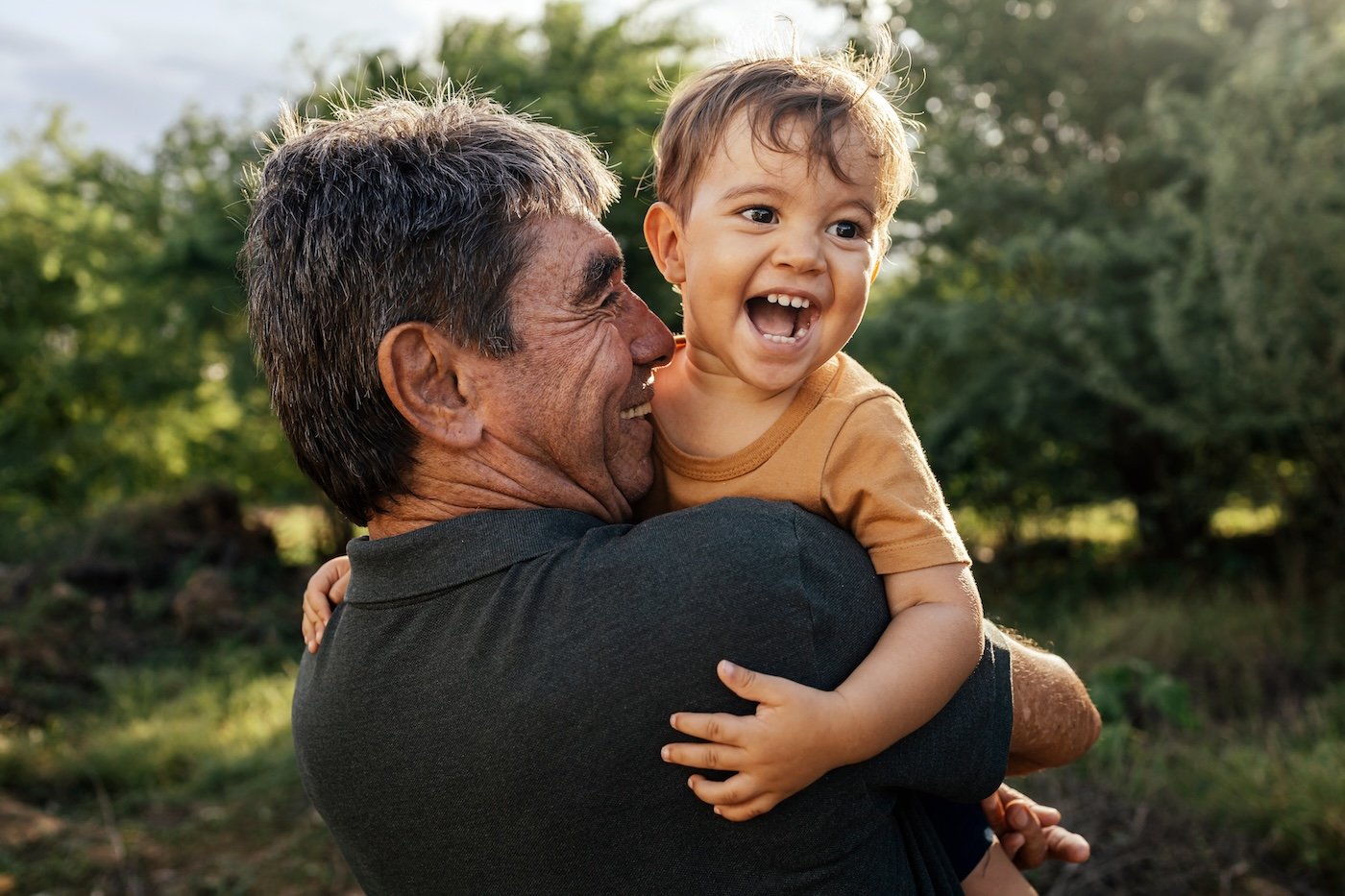 man smiling holding his grandson outside