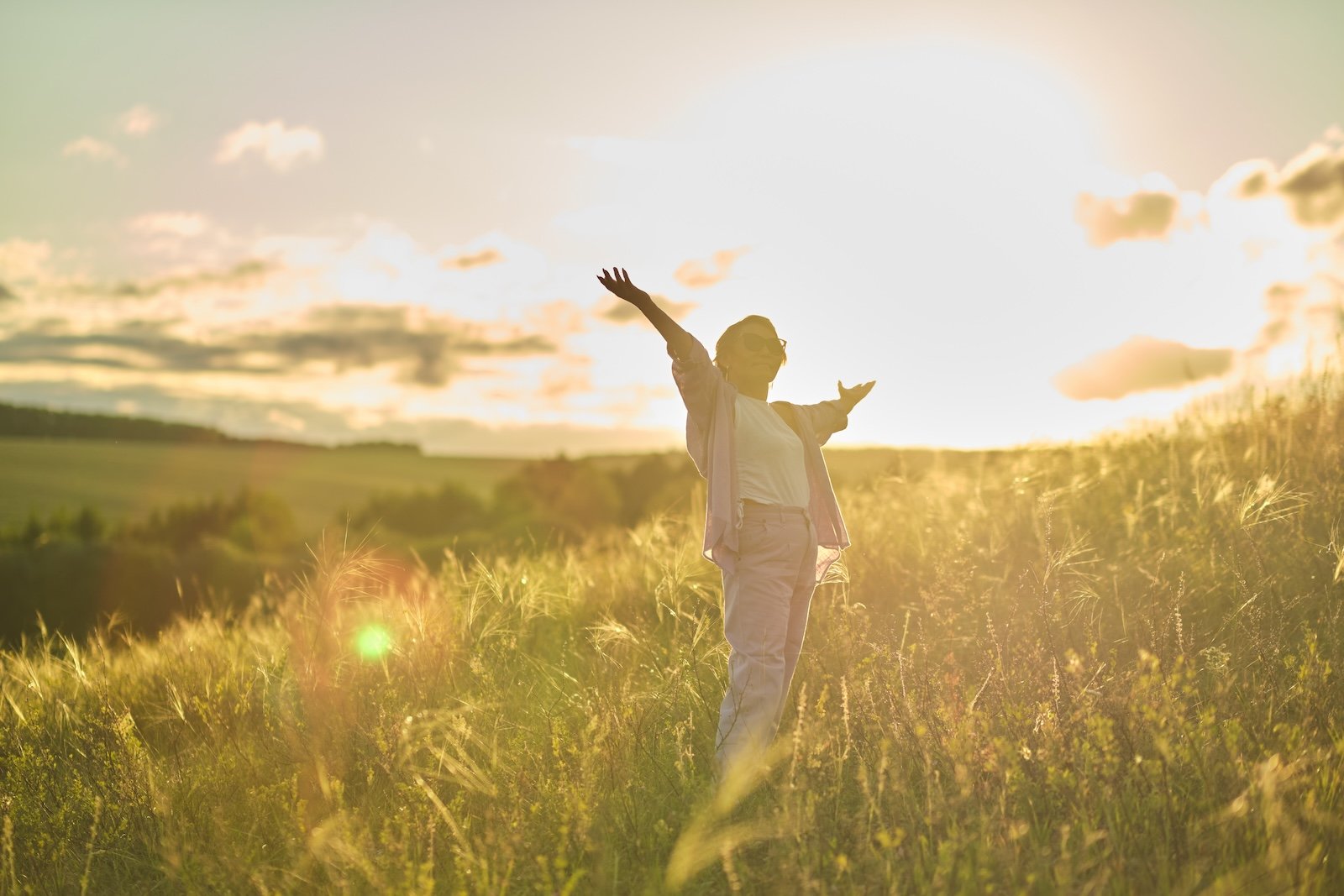 woman standing in sunny field with arms spread