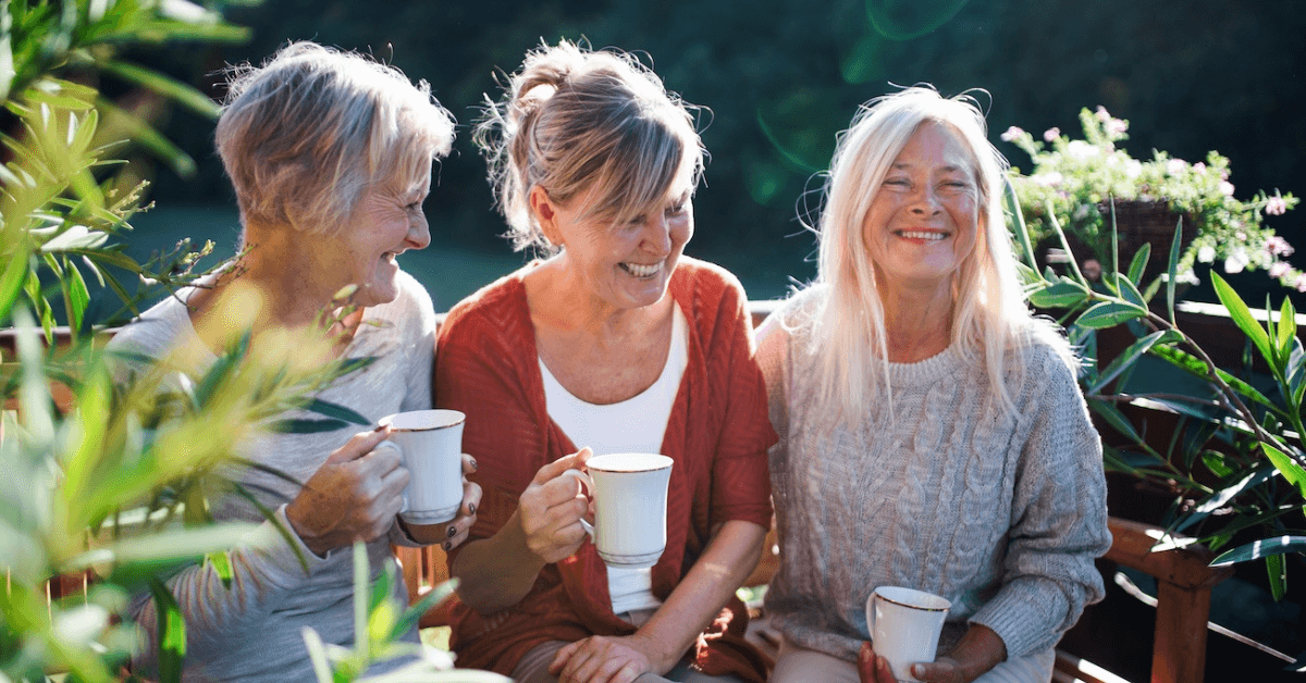 three women sitting on a bench drinking coffee outside