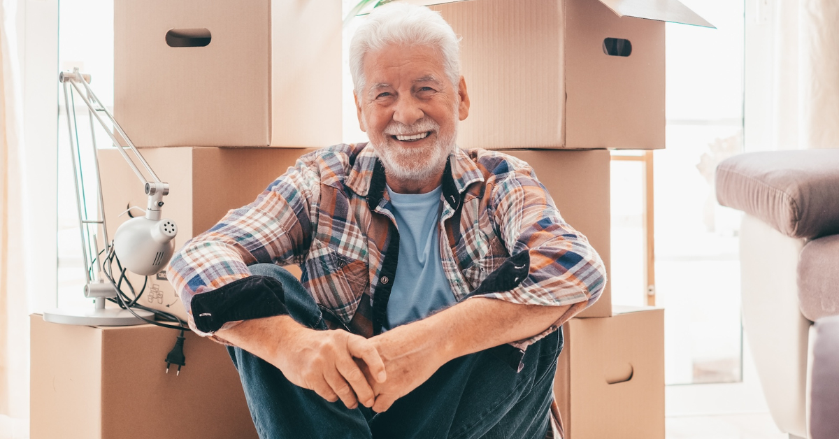 senior man smiling and sitting on floor in front of moving boxes