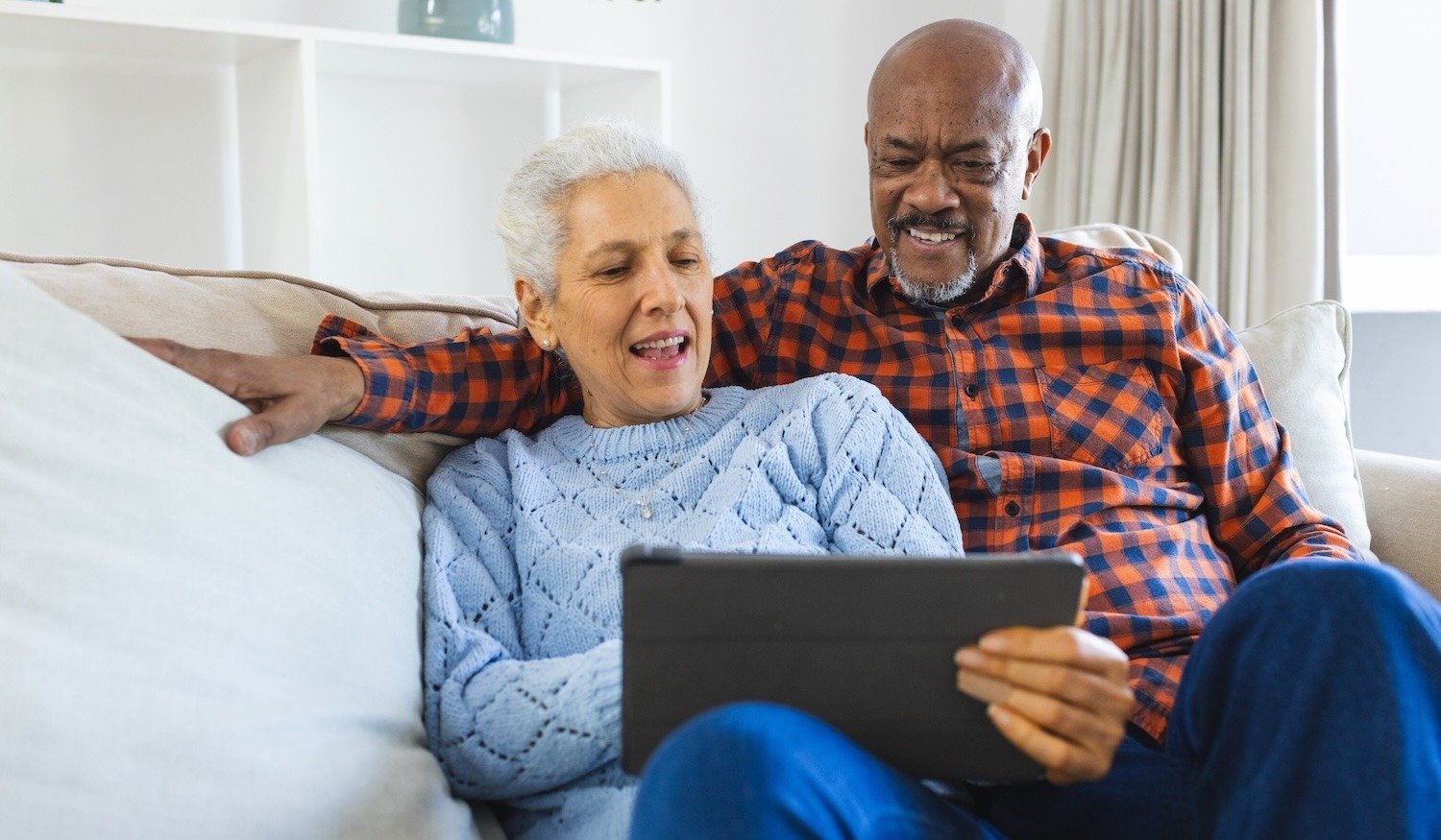 adult couple seated on couch using tablet to research senior living community options using online reviews 